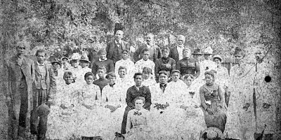 Juneteenth Celebration at Emancipation Park 1880 touched up. A group photograph of thirty-one people at a Juneteenth Celebration in Emancipation Park in Houston's Fourth Ward. Reverend Jack Yates is pictured on the left and Sallie Yates is pictured in the center toward the front in a black outfit
