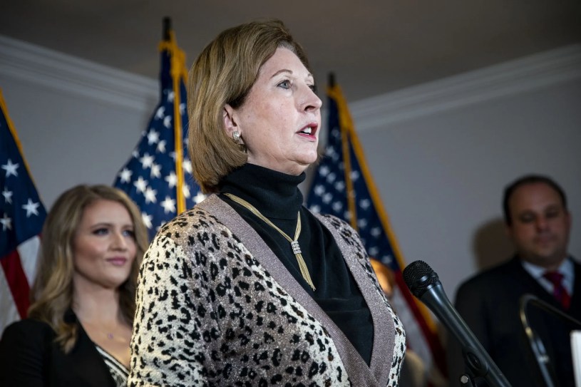Sidney Powell speaking at a press conference, gesturing with her right hand while standing behind a podium with the RNC logo.